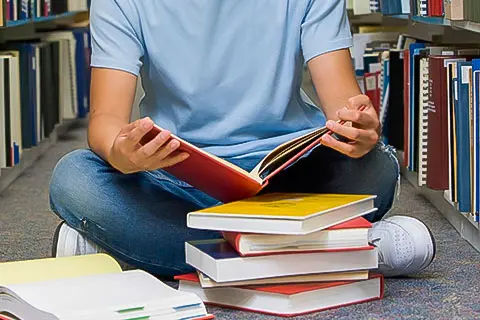 Jovem lendo livro em biblioteca